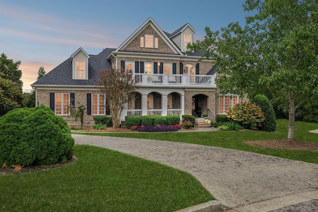 view of front of home with a shingled roof, a balcony, a porch, a front lawn, and brick siding