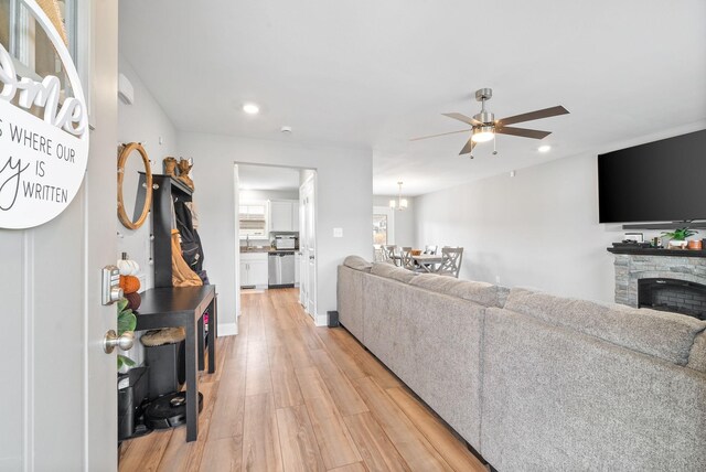 living area featuring baseboards, a ceiling fan, a stone fireplace, light wood-style floors, and recessed lighting