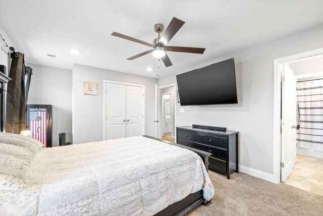 bedroom with a closet, light colored carpet, a ceiling fan, ensuite bath, and baseboards