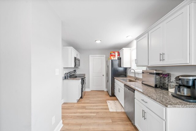 kitchen featuring light stone counters, stainless steel appliances, a sink, white cabinetry, and light wood-type flooring