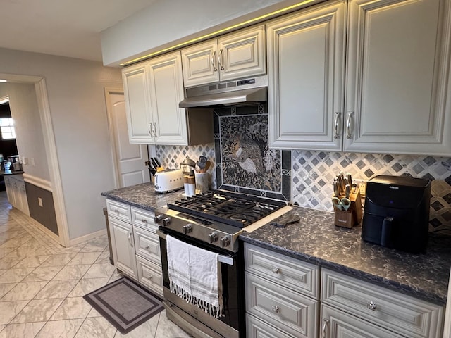 kitchen with under cabinet range hood, marble finish floor, backsplash, stainless steel gas stove, and dark stone countertops