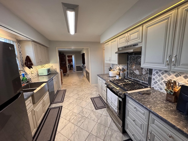 kitchen with stainless steel appliances, tasteful backsplash, a sink, dark stone countertops, and under cabinet range hood