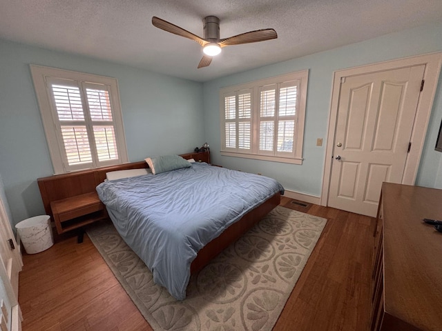 bedroom with a ceiling fan, visible vents, a textured ceiling, and wood finished floors