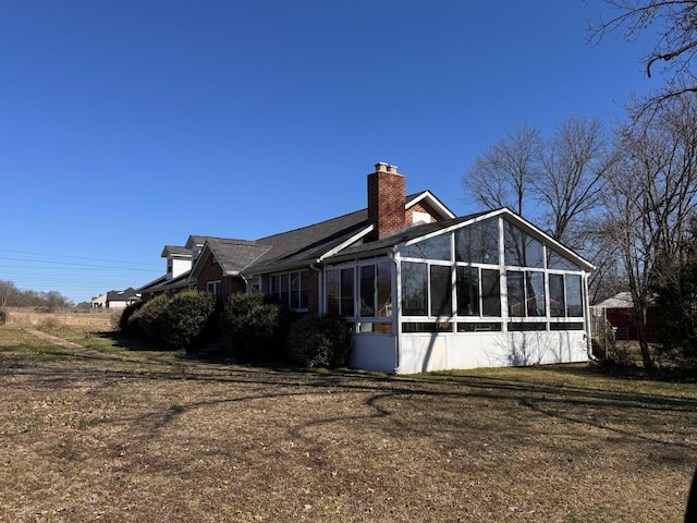 rear view of property featuring a yard, brick siding, a chimney, and a sunroom