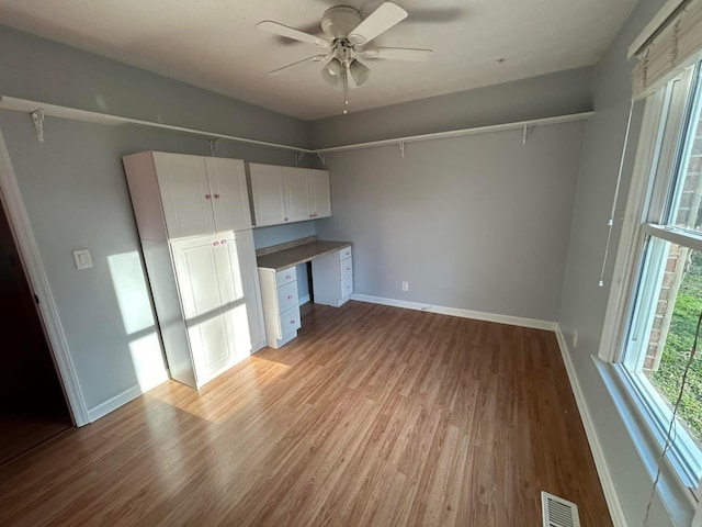 unfurnished bedroom with baseboards, visible vents, light wood-style flooring, ceiling fan, and built in desk