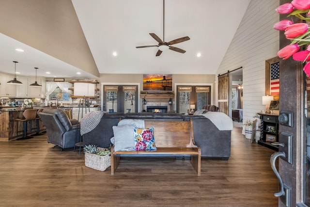 living area with dark wood-style floors, a lit fireplace, a barn door, and high vaulted ceiling