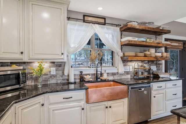 kitchen featuring tasteful backsplash, dark stone counters, appliances with stainless steel finishes, open shelves, and a sink