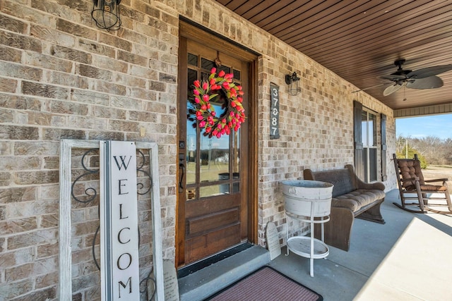 property entrance with a ceiling fan, covered porch, and brick siding