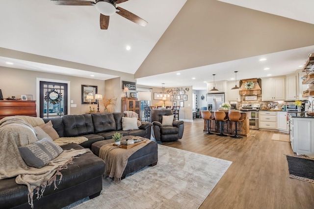 living room with high vaulted ceiling, recessed lighting, light wood finished floors, and ceiling fan with notable chandelier