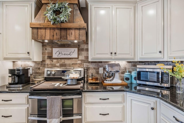 kitchen with dark stone counters, custom range hood, appliances with stainless steel finishes, white cabinetry, and backsplash