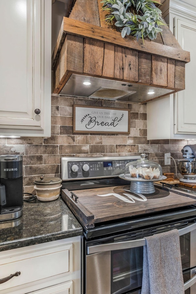 kitchen featuring range with two ovens, white cabinets, tasteful backsplash, dark stone countertops, and custom range hood