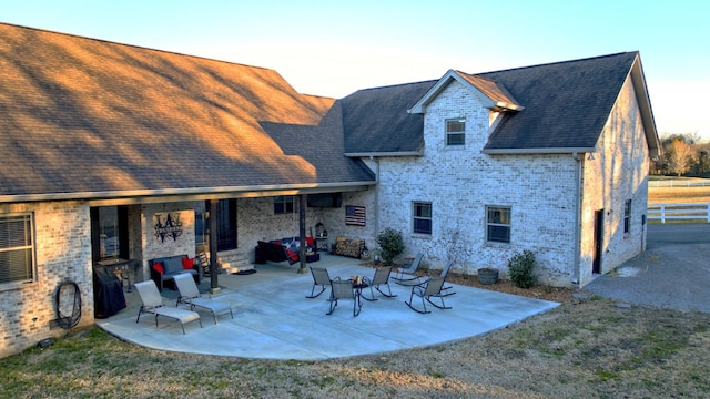 rear view of house featuring a patio area, roof with shingles, and brick siding