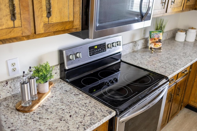 kitchen with light stone countertops, appliances with stainless steel finishes, and brown cabinetry