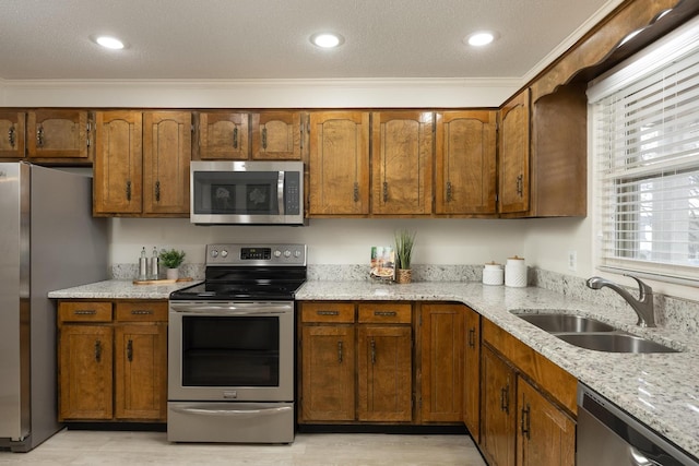 kitchen featuring brown cabinetry, light stone counters, stainless steel appliances, and a sink