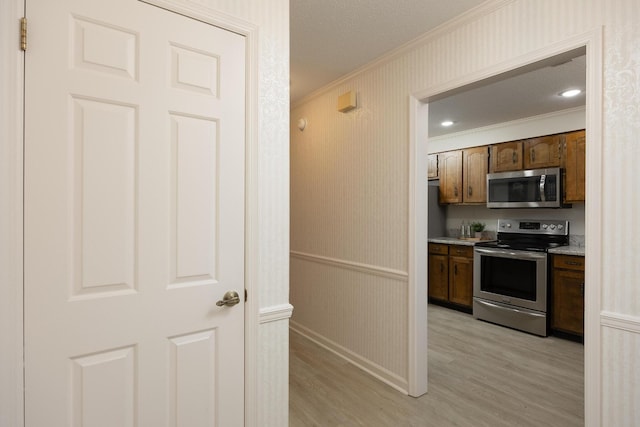 kitchen featuring a wainscoted wall, crown molding, light wood finished floors, stainless steel appliances, and wallpapered walls