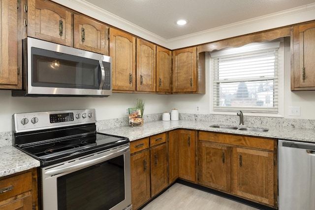 kitchen with crown molding, appliances with stainless steel finishes, brown cabinetry, and a sink