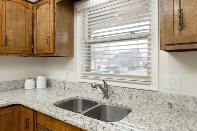 kitchen featuring brown cabinetry, a sink, and light stone countertops