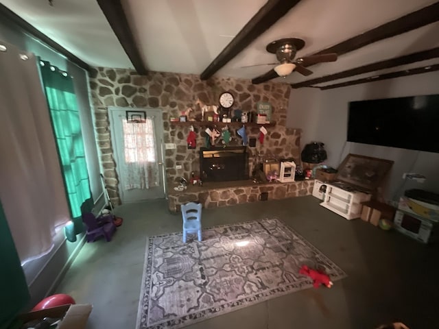 living area featuring ceiling fan, a stone fireplace, and beam ceiling