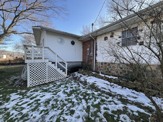 view of snow covered exterior with brick siding and stairway