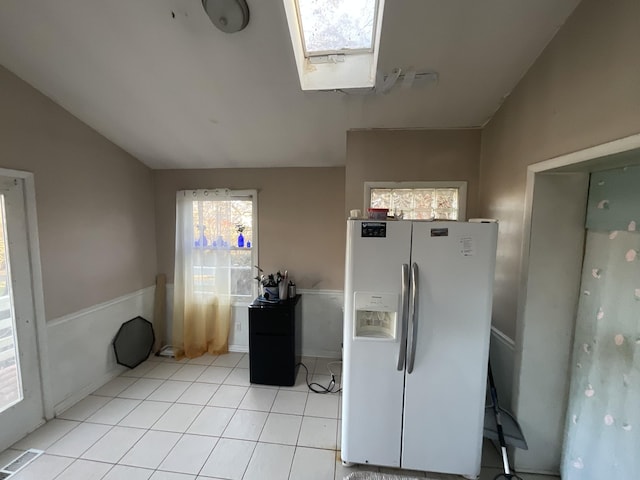 kitchen featuring light tile patterned floors, white fridge with ice dispenser, lofted ceiling with skylight, and visible vents