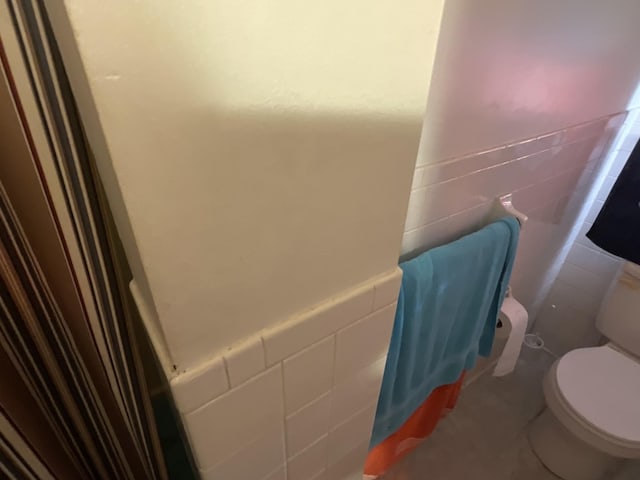 bathroom featuring wainscoting, tile walls, and toilet