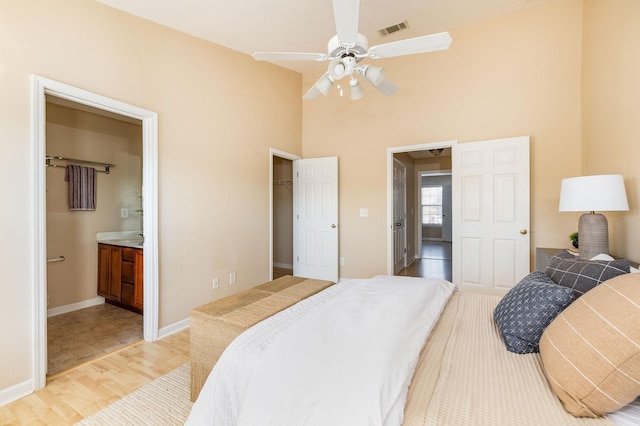 bedroom with baseboards, visible vents, connected bathroom, a high ceiling, and light wood-style floors