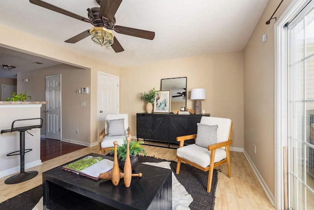 living room with a ceiling fan, light wood-style flooring, and baseboards