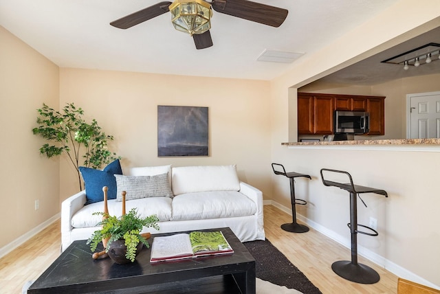 living room featuring light wood-style floors, baseboards, and a ceiling fan