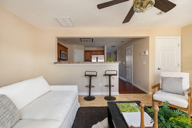 living area with a ceiling fan, visible vents, baseboards, and wood finished floors