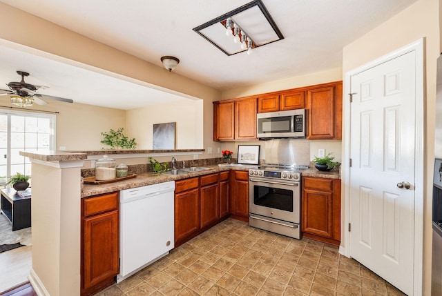 kitchen with appliances with stainless steel finishes, brown cabinetry, a ceiling fan, a sink, and a peninsula