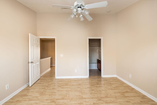 unfurnished bedroom featuring a ceiling fan, baseboards, a spacious closet, a closet, and light wood-type flooring