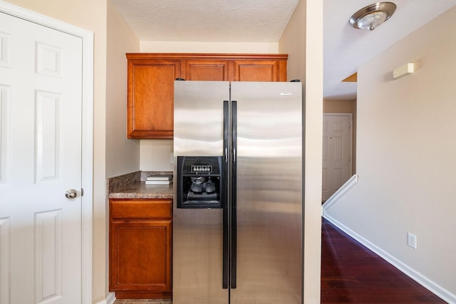 kitchen featuring a textured ceiling, dark wood-type flooring, stainless steel fridge with ice dispenser, brown cabinetry, and dark countertops