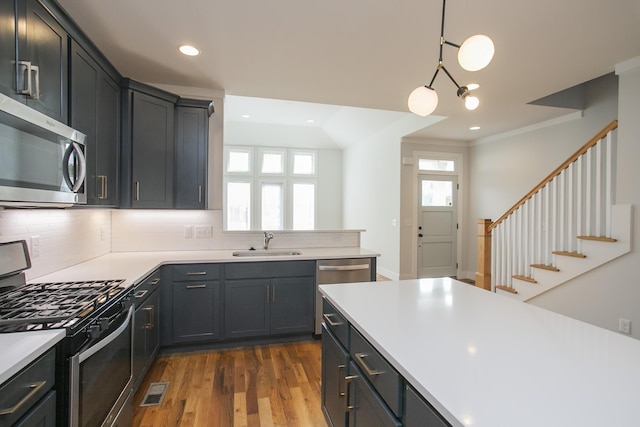 kitchen featuring stainless steel appliances, tasteful backsplash, light countertops, hanging light fixtures, and a sink