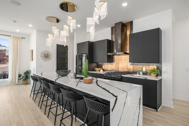 kitchen with black gas range, wall chimney exhaust hood, tasteful backsplash, and hanging light fixtures