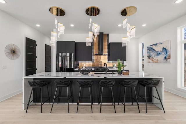 kitchen featuring decorative light fixtures, a large island, a breakfast bar area, freestanding refrigerator, and wall chimney exhaust hood