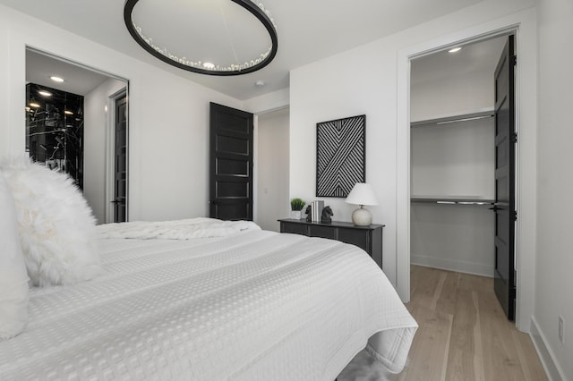 bedroom with a spacious closet, a closet, light wood-style flooring, and baseboards