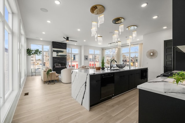 kitchen featuring black appliances, a kitchen island with sink, pendant lighting, and dark cabinets