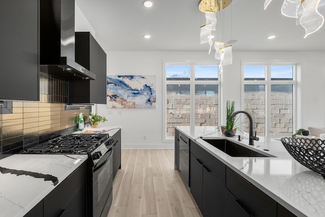 kitchen featuring wall chimney exhaust hood, dark cabinets, hanging light fixtures, black appliances, and a sink