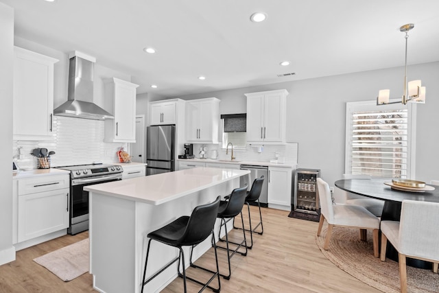 kitchen with wine cooler, stainless steel appliances, a sink, wall chimney range hood, and a kitchen island