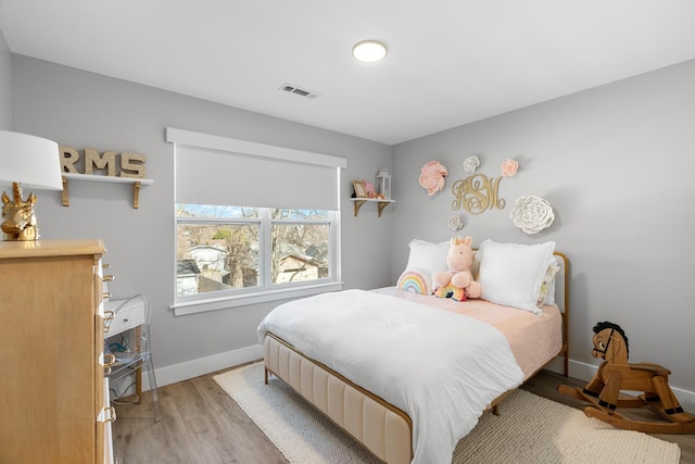 bedroom with light wood finished floors, visible vents, and baseboards