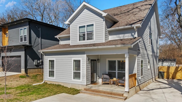 rear view of property featuring covered porch, a shingled roof, fence, and concrete driveway