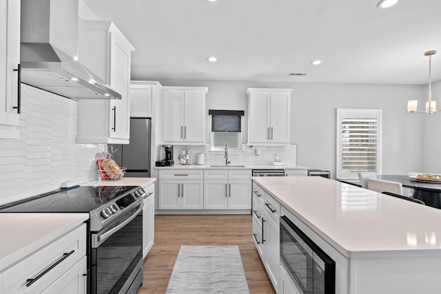 kitchen with a sink, visible vents, white cabinetry, appliances with stainless steel finishes, and wall chimney range hood