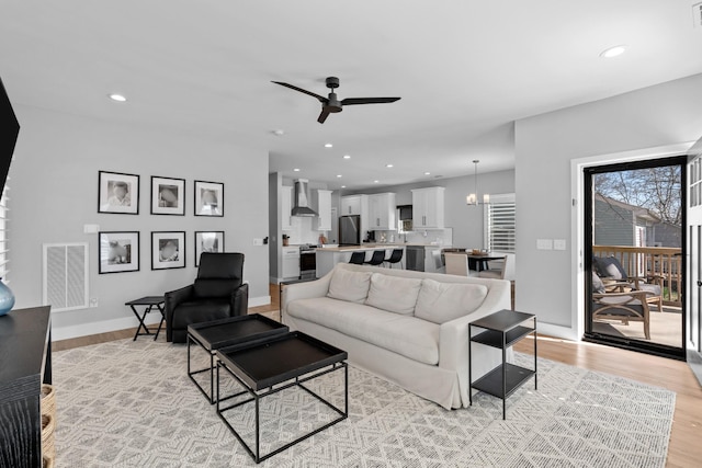 living area featuring recessed lighting, light wood-style flooring, visible vents, and ceiling fan with notable chandelier