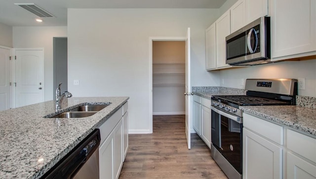 kitchen with visible vents, white cabinets, appliances with stainless steel finishes, light stone countertops, and a sink