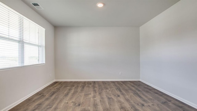 empty room featuring dark wood-type flooring, visible vents, and baseboards