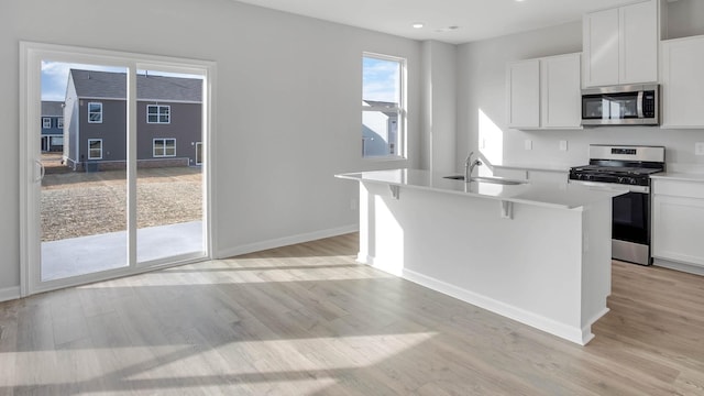 kitchen featuring appliances with stainless steel finishes, a kitchen island with sink, light countertops, white cabinetry, and a sink