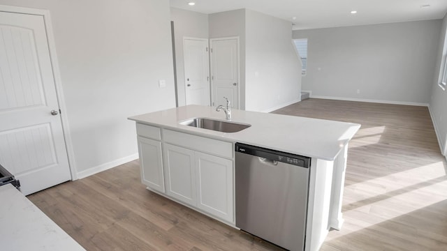 kitchen featuring light countertops, stainless steel dishwasher, a kitchen island with sink, a sink, and white cabinetry