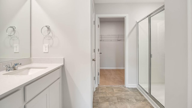 bathroom with a walk in closet, stone finish floor, a shower stall, vanity, and baseboards