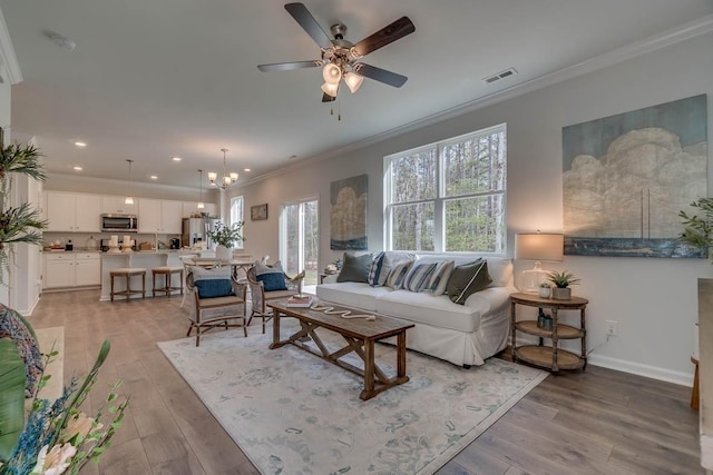 living area with ornamental molding, baseboards, visible vents, and light wood finished floors