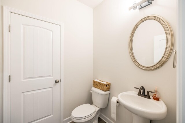 half bath with toilet, baseboards, and a sink